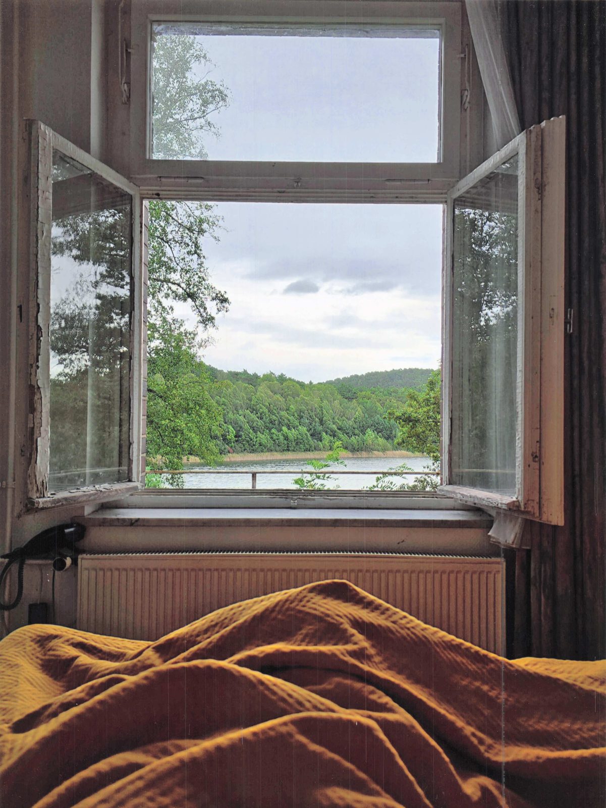 Hotelzimmer mit goldenem Bettüberwurf, offenes Fenster mit Blick auf den See